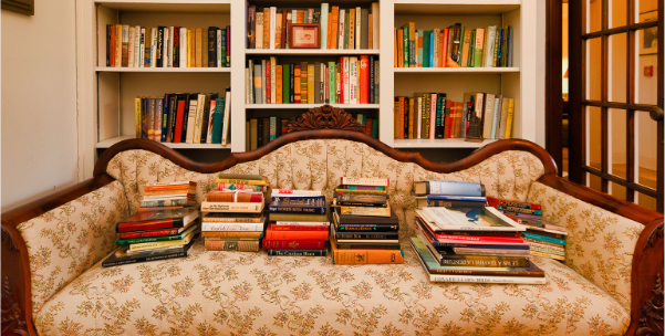 Stacks of books on an antique couch in front of the bookshelves in the Eudora Welty house living room.