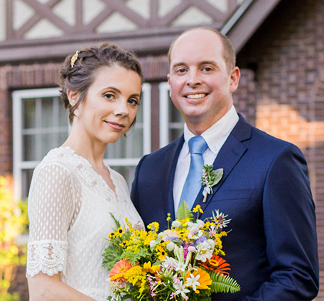A bride and groom holding a wedding bouquet in front of the Welty House at the Eudora Welty House & Garden.