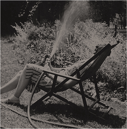 Black-and-white photo of Eudora Welty watering the upper garden while lounging in a lawn chair.