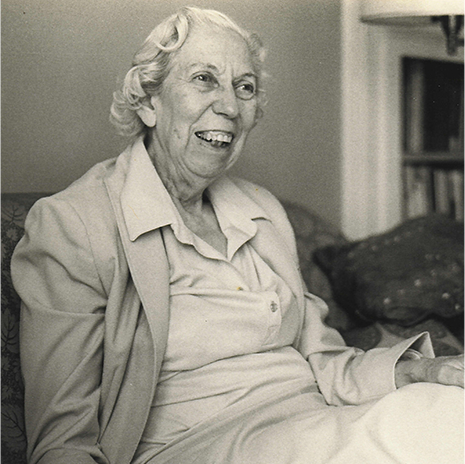Author Eudora Welty in her later years, seated indoors and laughing, in a dress and blazer.
