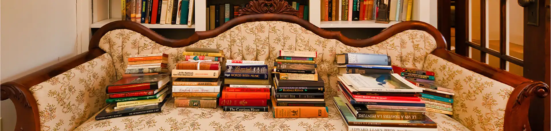 Stacks of books on an antique couch in front of the bookshelves in the Eudora Welty house living room.