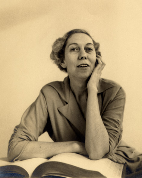 Eudora Welty as a young woman seated behind a large open book, with one arm folded across the pages and one hand at her cheek.