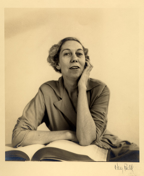 Portrait of Eudora Welty as a young woman seated behind a large open book, with one arm folded across the pages and one arm under her chin, photographed by Kay Bell.