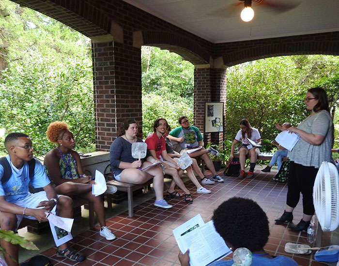 A teacher leads a diverse group of high school students in an educational activity on the porch at the Eudora Welty House & Garden.